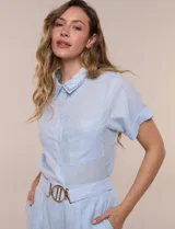 Conjunto de dos piezas de lino celeste, compuesto por una camisa de manga corta con cuello bordado y bolsillos en el pecho, y un pantalón palazzo de tiro alto con cinturón con hebilla dorada.