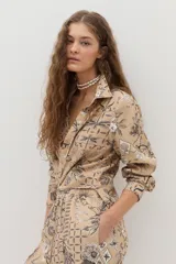 Camisa beige de manga larga, con cuello camisero, cierre frontal con botones y un estampado detallado de motivos botánicos e insectos en tonos oscuros.