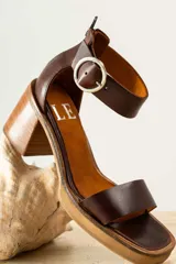 Sandalias de cuero color marrón con tira ancha sobre los dedos y tira con hebilla al tobillo. Tacón de madera.