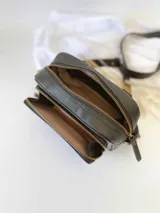 Bandolera de cuero negro con textura grabada tipo cocodrilo en el frente y laterales lisos. Cuenta con doble compartimento con cierre metálico, correa larga ajustable y etiqueta de cuero natural con logo grabado.