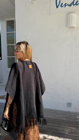 Ruana negra de tejido liviano con terminación de flecos en el ruedo y mangas amplias.