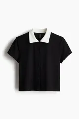 Camisa de manga corta acanalada de color negro con cuello y botonadura frontal en contraste de color blanco.