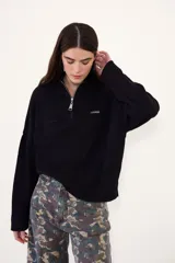Sweater negro de punto con cuello alto y cierre frontal parcial de cremallera, de manga larga y diseño holgado con hombros caída.