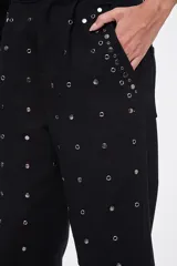 Pantalón negro de corte carrot, con bolsillos laterales, cierre frontal y aplicación de tachas metálicas en toda la prenda y en los dobladillos.
