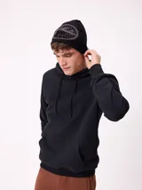 Gorro tipo beanie de punto color negro con diseño gráfico circular en gris en la parte frontal.