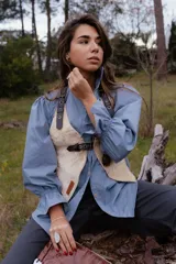 Camisa de algodón color azul, con silueta relajada, cuello camisero y mangas largas abullonadas con puños elásticos. Presenta cierre frontal con botones de madera.