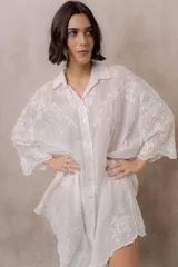 Camisola blanca de silueta amplia y caída liviana, con bordados florales sutiles, cuello camisero, cierre frontal de botones y mangas 3/4.
