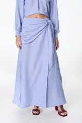 Falda larga celeste con finas rayas verticales blancas, corte evasé y detalle de nudo drapeado en la cintura.