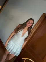 Vestido corto negro con escote en V profundo, estilo halter con tiras para atar al cuello. Presenta un diseño ajustado en el busto con tiras ajustables bajo el mismo que se cruzan y anudan en la espalda, y falda con volado en el ruedo con detalle de encaje.