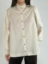 Camisa color celeste con cuello mao y mangas largas abullonadas. Presenta cierre frontal con botones y detalle de costuras en hombros y ruedo.