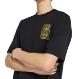 Remera Adidas de manga corta, color negro, con cuello redondo y diseño holgado. Presenta un parche rectangular dorado con el logo de la marca en el pecho.