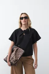 Top negro de manga corta con detalle de nudo en el escote y abertura tipo gota. Presenta una silueta relajada y textura sutil en la tela.