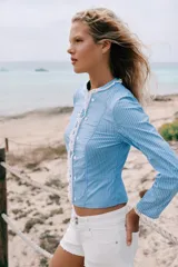 Chaqueta de popelín a rayas celestes y blancas, con cuello redondo y mangas largas. Presenta detalles de encaje a contraste en el cuello, los puños y la botonadura frontal, la cual cuenta con cierre de botones.