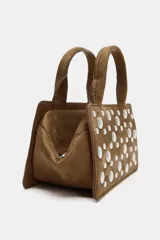 Bolso de mano estructurado color marrón, confeccionado en material tipo gamuza, con detalle de tachas metálicas plateadas en el frente. Cuenta con doble asa de mano, asa bandolera extraíble, cierre superior con cremallera y bolsillo interior.