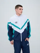 Campera deportiva Umbro modelo Beat, confeccionada en nylon ligero con diseño de bloques de color en blanco, azul marino y verde azulado. Presenta cierre frontal, cuello alto y elásticos en puños y cintura.