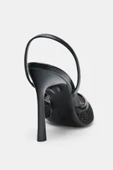 Zapato destalonado de tacón alto fino, color negro, con cuerpo principal de rejilla y puntera afilada. Presenta ribetes en material liso y tira trasera elástica para ajuste.