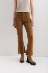 Pantalón de jean color marrón óxido, tiro medio, corte ajustado en muslos y ligeramente acampanado en la parte inferior (bootcut/flare), con bajo desflecado.