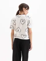 Remera de algodón pima blanco con estampado de corazones formados por cadenas, de calce regular, mangas murciélago y cuello redondo.