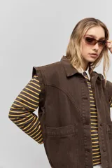 Chaleco de jean negro, de calce relajado con hombros caídos, cuello camisero, cierre frontal con botones y grandes bolsillos aplicados.