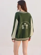 Cardigan oversize de punto color celeste con mangas largas verde oscuro, detalles de líneas rojas en la botonera y los puños, cierre frontal con botones y logo bordado en el pecho.