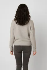 Sweater de tejido de punto color gris, con cuello redondo y mangas largas. Presenta detalle de tachas metálicas a lo largo de los hombros y la parte superior de las mangas.