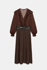 Vestido midi de color marrón con diseño combinado, escote en pico con volantes, mangas largas con puños elásticos y falda evasé. Incluye un cinturón negro con hebilla dorada en la cintura y cierre lateral con cremallera oculta.