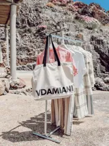 Bolso tipo tote bag de algodón color crudo con asas negras y estampado con la palabra "VDAMIAN" en letras negras grandes.