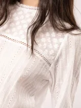 Blusa blanca de algodón con escote redondo, manga tres cuartos y silueta oversized. Presenta bordados y texturas combinadas.