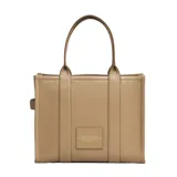 Bolso tipo tote de gran tamaño, confeccionado en cuero negro con textura granulada. Presenta el logo de la marca estampado en el frente con la inscripción The Tote Bag Marc Jacobs. Cuenta con asas superiores resistentes y un diseño espacioso.