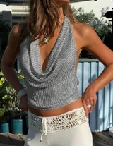 Top de tejido metálico plateado con diseño de cuello halter y escote profundo en V. Presenta una caída fluida y un acabado brillante ideal para eventos nocturnos.