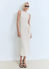Vestido midi de punto fino color beige, sin mangas, con cuello barco y diseño recto. Incluye un cinturón decorativo tejido a la altura de la cintura.