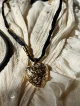 Collar con colgante de corazón dorado con detalles florales, con cinta de satén negra.