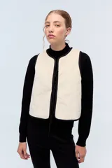 Chaleco color crudo de pana texturada con bordes negros, lazos de ajuste frontales y espalda lisa.