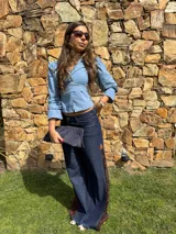Camisa celeste con escote en V, cuello solapa y detalle cruzado con lazo ajustable en la cintura. Cuenta con mangas 3/4 abullonadas y puños con detalle de volados.