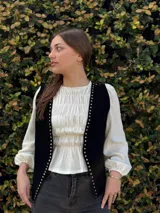 Chaleco de cuero negro con tachas metálicas doradas en los bordes frontales.