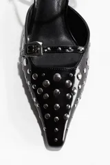 Sandalia de taco forrado, color negro charol, con punta fina. Presenta tira delantera y pulsera ajustable con hebilla, ambas decoradas con tachas metálicas plateadas.