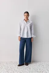 Camisa de algodón blanca, de calce relajado, con cuello clásico, mangas largas y cierre frontal con botones.