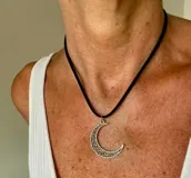 Gargantilla con tira negra y dije colgante plateado en forma de medialuna con diseño ornamentado.