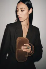 Bolso mini bowling color marrón de cuero gamuza, con doble asa de mano y correa bandolera extraíble. Tiene cierre de cremallera y bolsillo interior con cremallera.