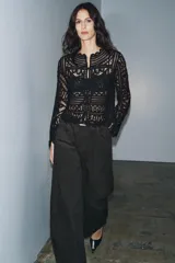 Blusa negra de manga larga confeccionada en tejido tipo crochet con intrincados patrones geométricos y florales. Presenta cuello redondo y cierre frontal con botones.