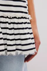 Remera oversize de punto rayada en blanco y negro, con cuello redondo, mangas cortas amplias y detalle de volado fruncido en el ruedo.