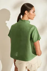 Blusa de lino verde de manga corta y corte recto, con cuello alto con volado y cierre frontal cruzado con botoncitos dorados.