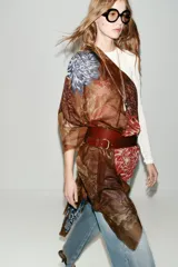 Pañuelo rectangular de gran tamaño con estampado floral de peonías en tonos azules y rosados sobre fondo marrón. Presenta bordes con acabado deshilachado.