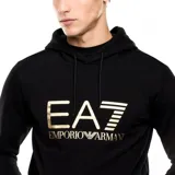 Sudadera con capucha (canguro) de color negro, corte estándar, con bolsillo canguro frontal. Presenta el logo grande de EA7 Emporio Armani en color dorado/beige en el pecho, con el texto 'EMPORIO ARMANI' debajo.