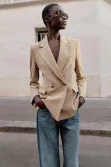 Blazer cruzado color beige, de manga larga, con cuello solapa y forro interior negro. Presenta cierre frontal con botones dorados y bolsillos de vivo en el pecho y bolsillos con solapa en el delantero.