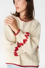 Sweater de punto color crudo con diseño de corazones rojos en las mangas, cuello redondo y terminaciones acanaladas en contraste rojo.