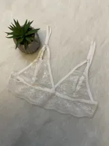 Conjunto de lencería de encaje blanco compuesto por un bralette triangular, una tanga con tiras y un portaligas integrado. El diseño presenta detalles de encaje floral y breteles regulables.