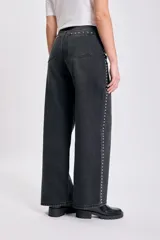 Pantalón de jean negro de corte recto y tiro alto, con detalle de tachas metálicas plateadas a lo largo de las costuras laterales.