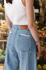 Jean de corte wide leg con diseño de tiro alto y piernas amplias. Presenta detalles de puntilla de crochet en los bolsillos delanteros y a lo largo de las costuras laterales, aportando un estilo romántico y distintivo.