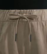 Pantalón jogger Marfinno color beige, confeccionado en suedine con cintura elástica y cordón ajustable. Presenta detalles perforados en los bolsillos laterales y en las costuras laterales, además de puños elásticos en los tobillos.